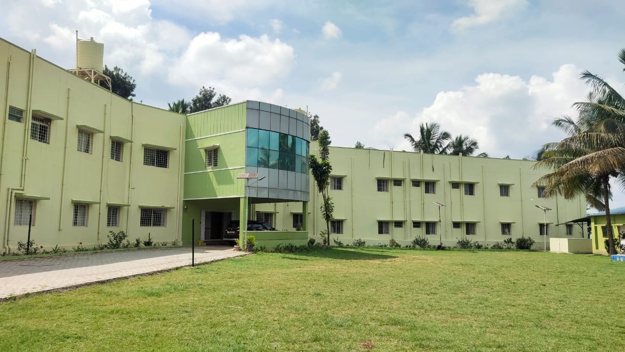 The MBBCS campus: green college buildings behind a lawn, under a bright sky